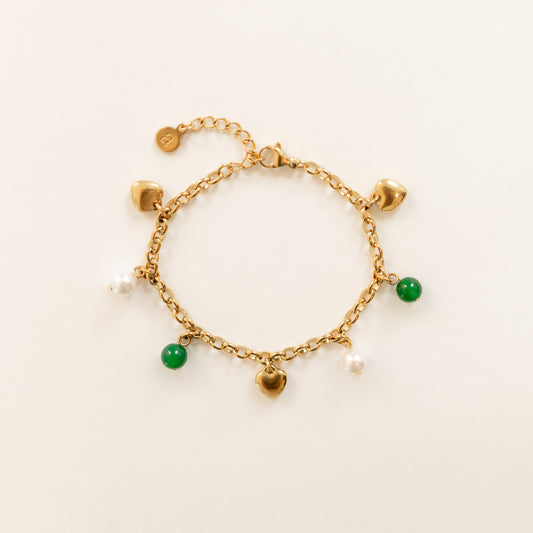 A gold 14k gold plated charm bracelet with dangling charms, including three small gold hearts, two green agate beads, and two white pearls, displayed on a clean off-white background.