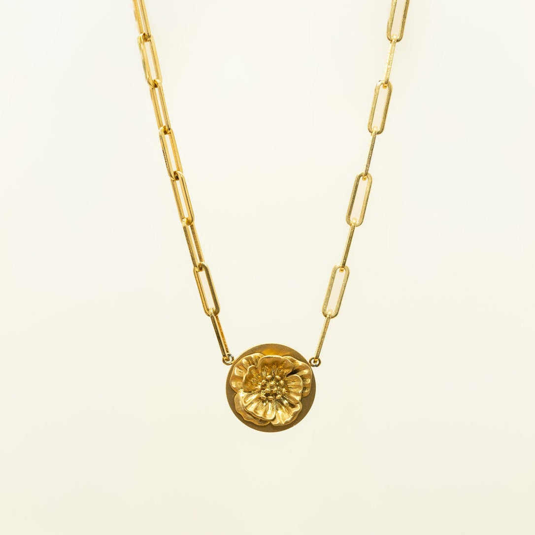 18k gold plated poppy necklace with round floral pendant and gold paperclip chain on a cream background.