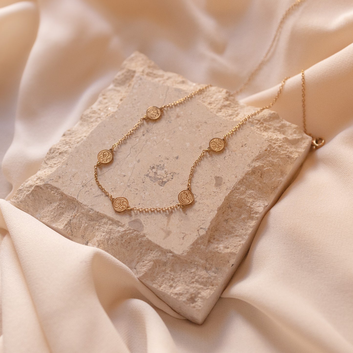 A gold chain bracelet inspired by the four corners of the Kaaba, featuring one black and three clear stones on a beige fabric background.