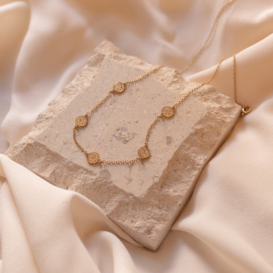 A gold chain bracelet inspired by the four corners of the Kaaba, featuring one black and three clear stones on a beige fabric background.
