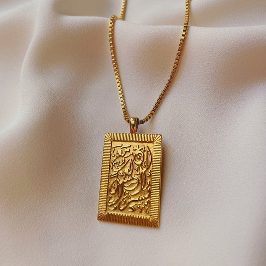 Gold perseverance necklace with square engraved pendant and rope chain displayed on soft cream fabric.