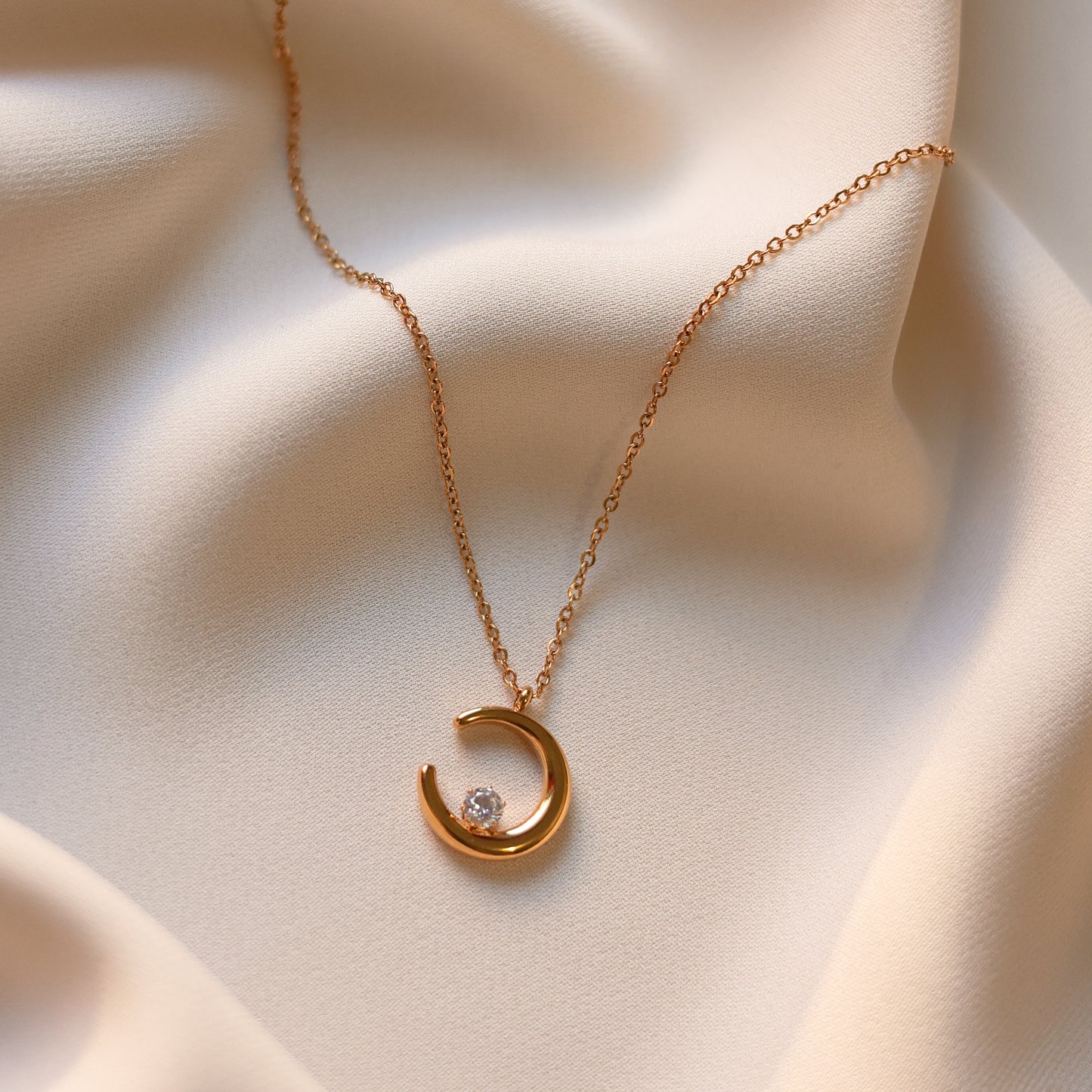 Gold plated moon necklace with crescent pendant and delicate chain displayed on soft cream fabric.