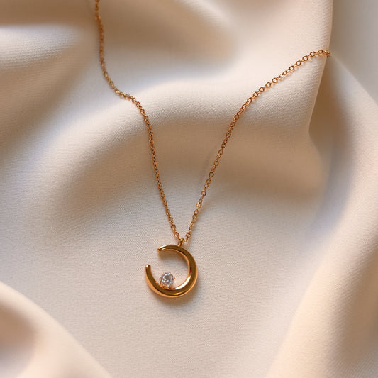 Gold plated moon necklace with crescent pendant and delicate chain displayed on soft cream fabric.