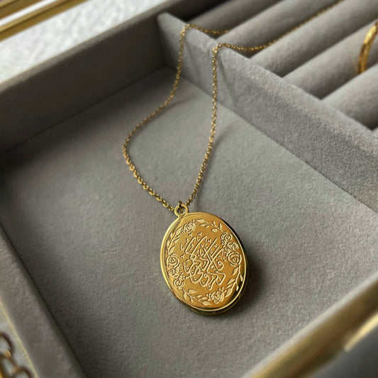 Gold remember me necklace with round engraved pendant and delicate chain displayed inside a soft gray jewelry box.